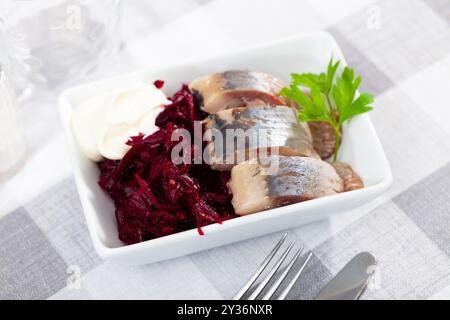Salade de hareng appétissante avec betteraves, crème sure et persil dans une assiette blanche Banque D'Images