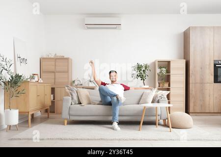 Bel homme allumant le climatiseur à la maison Banque D'Images