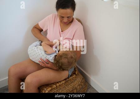 Une mère allaitant tendrement son bébé assis dans une pièce confortable. L'image capture la chaleur de l'affection maternelle et le lien intime entre eux Banque D'Images