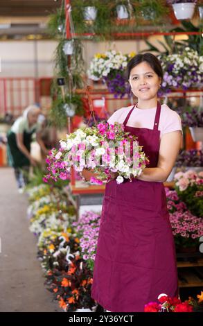 Vendeuse d'âge moyen tenant calibrachoa dans des pots de fleurs sur le marché des plantes en plein air Banque D'Images