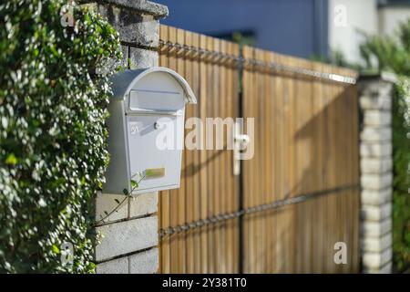 Boîte aux lettres en métal blanc ou boîte aux lettres montée sur un mur de briques à côté d'une entrée de maison en bois. Réglage nuit. Couvercle fermé pour lettres Banque D'Images