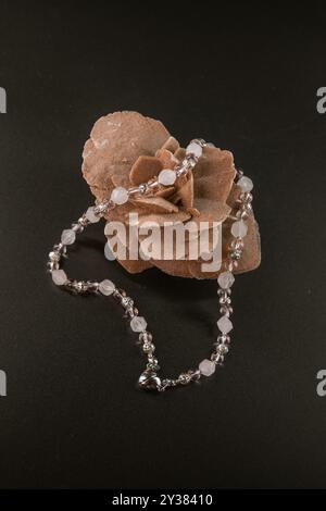 Collier de quartz rose clair et blanc avec un coeur métallique sur une pierre rose du désert sur fond noir, bijoux faits à la main Banque D'Images