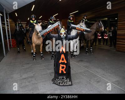 Un manifestant en costume tient un support de missile cassé lisant : « CESSEZ-LE-FEU MAINTENANT ! » Devant une ligne de chevaux de la police, Un blocus planifié et une manifestation contre les Forces terrestres 2024, la plus grande exposition de l'industrie de la défense dans l'hémisphère sud, ont éclaté en affrontements avec la police tout au long de la journée. Les manifestants qui tentaient d'empêcher l'entrée de la convention ont jeté des objets et des liquides sur les officiers, construit de petits barrages et déclenché des incendies d'ordures, tandis que la police a utilisé la force, le gaz poivre, les gaz lacrymogènes, les grenades paralysantes et les balles en caoutchouc sur les manifestants Banque D'Images