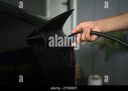 Gros plan d'un homme branchant un câble de charge dans un véhicule électrique ou à la maison. Concept de transport respectueux de l'environnement Banque D'Images