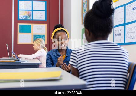 À l'école, deux filles afro-américaines parlent et sourient tandis qu'une autre fille utilise un ordinateur portable Banque D'Images