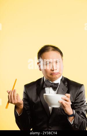 Homme, baguettes et portrait en studio avec visage drôle, smoking et confondu avec bol par fond. Personne chinoise, conteneur et bande dessinée pour la nutrition Banque D'Images