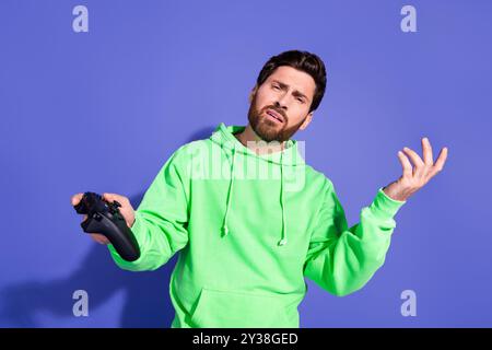 Portrait photo d'un bel homme funky d'âge mûr portant un sweat à capuche vert jouant à des jeux insatisfait perdant isolé sur fond de couleur violette Banque D'Images