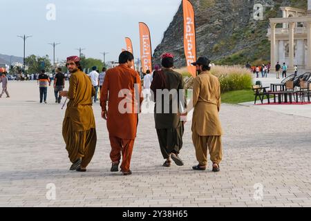 Vue arrière du groupe de 4 jeunes hommes migrants du moyen-Orient portant un tissu traditionnel décontracté marchant sur la rue Khor Fakkan. Banque D'Images