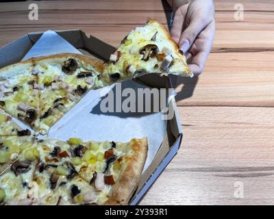 La main d'une femme sort un morceau de pizza de la boîte Banque D'Images