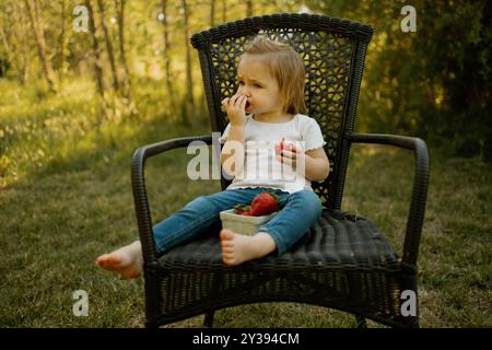 Enfant en bas âge mangeant un panier de fraises à l'extérieur Banque D'Images