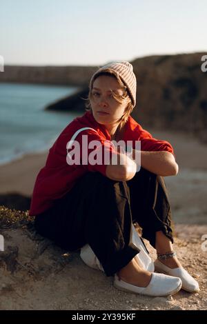 Femme assise sur une falaise rocheuse au coucher du soleil à Sagres, Algarve, Portugal. Banque D'Images