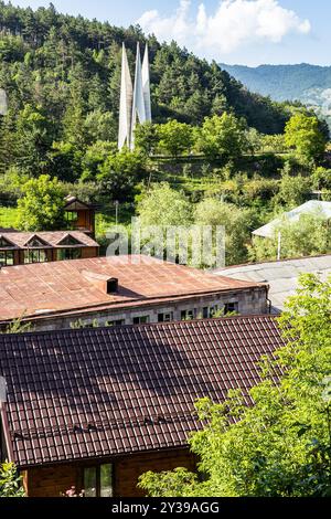 Maisons de la ville de Dilijan, Arménie avec Monument au 50e anniversaire de l'établissement du pouvoir soviétique en Arménie sur la pente verte de montagne ensoleillée su Banque D'Images