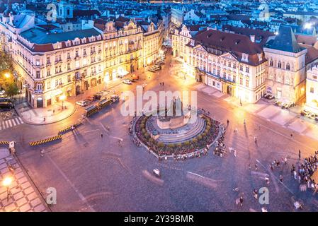 À la tombée de la soirée, la place de la vieille ville de Prague prend vie avec des lumières vibrantes, projetant une lueur chaleureuse sur les bâtiments historiques et la foule animée rassemblée autour de la fontaine centrale. Banque D'Images