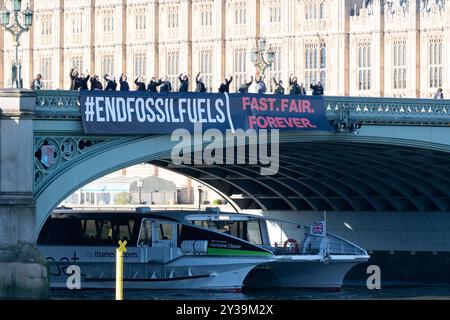 Londres, Royaume-Uni. 13 septembre 2024. Une grande bannière déclarant « mettre fin aux combustibles fossiles » est lâchée sur le pont de Westminster, par les chambres du Parlement, marquant le lancement de ce que les organisateurs prétendent être la plus grande action mondiale jamais entreprise pour exiger que les gouvernements travaillent pour mettre fin à l'utilisation des combustibles fossiles. La semaine d’action, du 13 au 20 septembre, voit la campagne Global Fight to End Fossil Fuels unir ses forces à la campagne Pay Up for Climate Finance pour exiger une élimination juste et équitable des combustibles fossiles comme moyen nécessaire pour lutter contre les menaces du chauffage mondial. Crédit : Ron Fassbender/Alamy Live News Banque D'Images