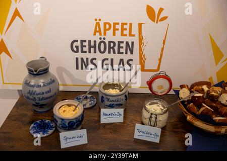 Hanau, Allemagne. 13 septembre 2024. Un Bembel traditionnel (l), un pichet en grès pour le cidre et des pâtes à tartiner de style Hesse, y compris le Spundekäs, sont présentés sur un buffet. Les producteurs de cidre ouvrent la saison 2024 sous la devise « les pommes appartiennent à un verre ». Crédit : Helmut Fricke/dpa/Alamy Live News Banque D'Images