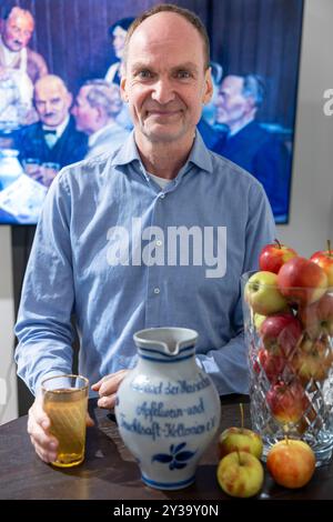 Hanau, Allemagne. 13 septembre 2024. Martin Heil, président de l’Association des presses à cidre de Hesse et à jus de fruits, se tient derrière un traditionnel Bembel, une cruche en grès pour cidre, avec un verre dubbe rempli de cidre. Les producteurs de cidre ouvrent la saison 2024 sous la devise « les pommes appartiennent à un verre ». Crédit : Helmut Fricke/dpa/Alamy Live News Banque D'Images