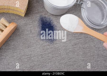 Une main de femme utilisant des ingrédients naturels bicarbonate de soude pour enlever les taches d'encre sur la sellerie texturée grise d'un canapé ou d'un tapis. vue de dessus Banque D'Images