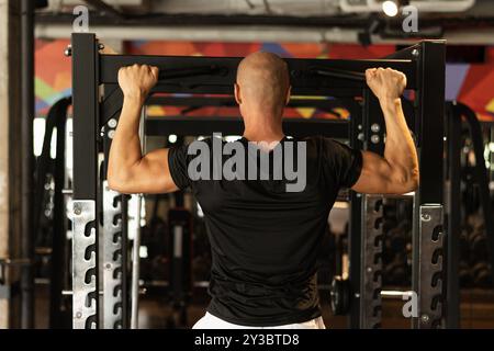 Homme de sport faire des tractions sur la barre horizontale au gymnase. Entraînement. Vue arrière. Banque D'Images