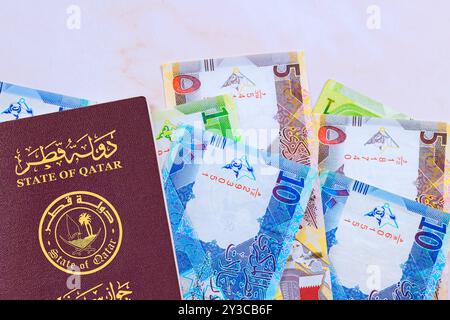 Passeport de l'État du Qatar délivré avec des billets de banque qatariens en monnaie riyals cash en différentes coupures Banque D'Images