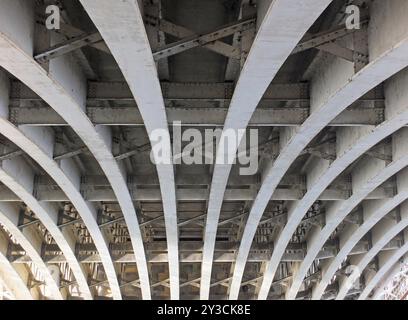 Vue en perspective de poutres en acier en forme d'arc courbé sous un vieux pont routier avec rivets et entretoises peints en gris Banque D'Images