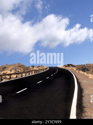 Une route vide à deux voies courbant vers l'horizon dans un paysage désertique accidenté avec un ciel nuageux bleu Banque D'Images