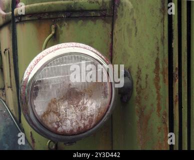 Gros plan du phare d'un vieux camion abandonné avec une grille et des panneaux verts rouillés Banque D'Images