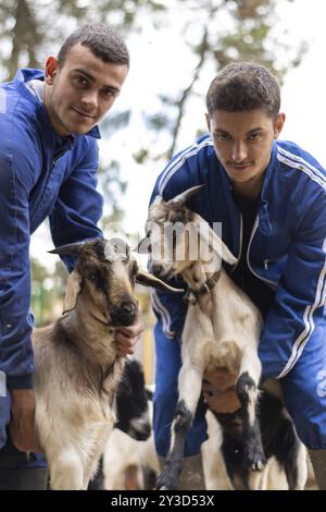 Portrait vertical de deux jeunes éleveurs avec leurs chèvres dans leur cour de ferme. concept de jeunes travaillant dans l'élevage et l'agricul Banque D'Images