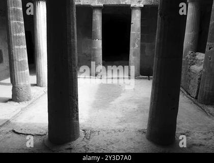 Image monochrome d'une chambre souterraine sur les tombes des rois à paphos chypre avec de vieilles colonnes de grès érodées entourant une porte vide sombre Banque D'Images