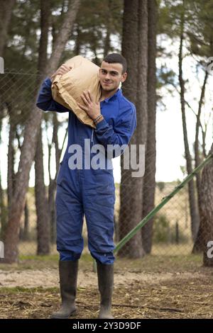 Portrait de jeune fermier souriant avec un sac de nourriture sur son épaule sur sa ferme et regardant la caméra., fond nature vertical Banque D'Images