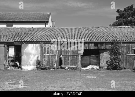 Image monochrome d'un atelier rural maculé réparé et réparé hors des bâtiments avec des portes en bois brisées minutieuses avec des déchets de peinture rouge délavée Banque D'Images