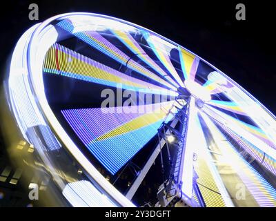 Un flou de mouvement de longue exposition d'une grande roue en rotation la nuit illuminé dans des couleurs néon vives Banque D'Images