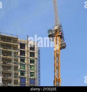 Une grande grue jaune travaillant sur un grand bâtiment à plusieurs étages en construction Banque D'Images