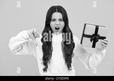 Visage en colère, émotions bouleversées de la jeune fille. Enfant jeune fille avec cadeau sur fond jaune isolé. Anniversaire, cadeau de vacances concept. Banque D'Images