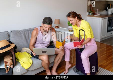 Joyeux jeune couple réservant leur voyage en ligne et se préparant avec enthousiasme pour leurs vacances d'été. Réservation en ligne de voyage à l'aide d'un ordinateur portable. Banque D'Images