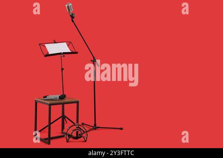 Stand avec notes de musique, microphone et tambourin sur fond rouge Banque D'Images