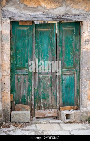 Volets en bois vieux et battus par les intempéries de style chic et shabby avec peinture écaillée et écaillée sur un bâtiment de village rustique en Grèce. Banque D'Images