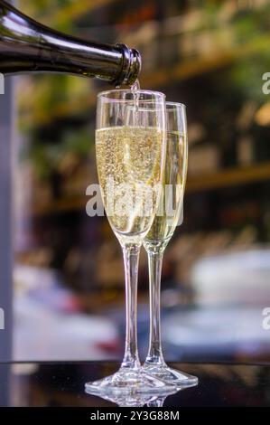 Deux verres de champagne ou de vin mousseux sur la table, dans l'un des verres le vin est versé de la bouteille sur un fond vert Banque D'Images