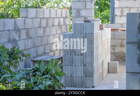 Une pile de blocs de cendre de béton est installée pour la construction dans la cour arrière, avec un peu de verdure et des arbres visibles autour Banque D'Images