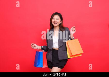 indonésie bureau expression de femme heureux candide portant sacs en papier shopping portant veste habillée sur fond rouge. pour les applications commerciales, lifestyle et s Banque D'Images