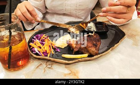 Portrait de mains de femme collectant des khubus (pain pita) accompagné de poulet rôti au four, nourriture arabe typique avec une fourchette et un couteau sur une assiette à Banque D'Images
