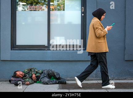 Montréal, Québec, Canada. 12 septembre 2024. Une femme passe devant un sans-abri. Au cours des dernières années, notre dépendance à l'écran a considérablement augmenté. L’une des raisons en est l’avancée rapide des technologies, tandis qu’une autre raison est les interactions sociales limitées engendrées par la pandémie. Des facteurs tels que l'utilisation excessive d'appareils numériques pour les réunions virtuelles et la socialisation ont encore aggravé la situation. (Crédit image : © Serkan Senturk/ZUMA Press Wire) USAGE ÉDITORIAL SEULEMENT! Non destiné à UN USAGE commercial ! Banque D'Images