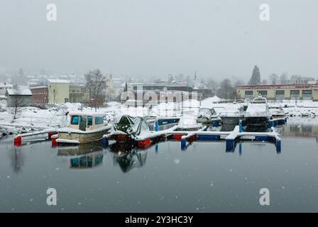 Un port calme dispose de bateaux reposant sur des quais colorés tandis que les flocons de neige tombent doucement, créant une atmosphère hivernale sereine dans cette scène pittoresque. Banque D'Images