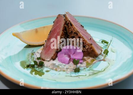 Thon poêlé gourmand avec fleur comestible et tranche de citron garni sur une élégante assiette en céramique. Banque D'Images