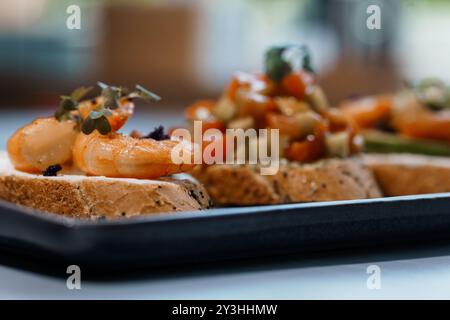 Délices gastronomiques de Bruschetta avec des garnitures de crevettes et de légumes disposées sur une élégante assiette noire. Banque D'Images