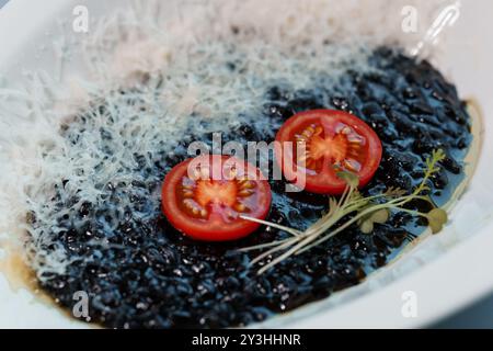 Risotto de riz noir gourmand avec tranches de tomates et Microgreens garnis de parmesan. Banque D'Images