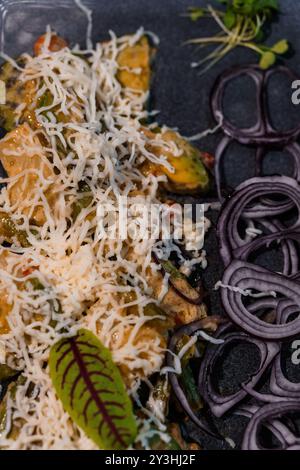 Sauté de légumes gourmet avec fromage râpé et oignons frais sur assiette Dark. Banque D'Images