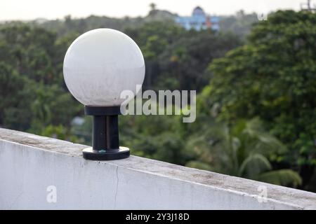 Lampe en verre rond blanc sur un poteau en acier noir monté sur le mur, fond naturel flou. Banque D'Images