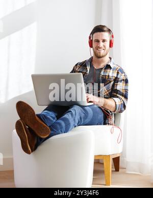 Homme, maison et sourire sur ordinateur portable avec casque pour éditer des vidéos en tant que vidéaste avec travail à distance. Personne masculine, employé et heureux sur portrait comme Banque D'Images