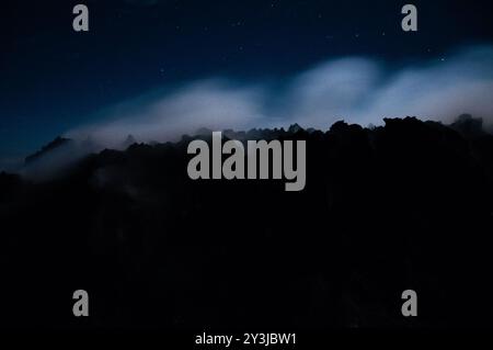 Vue nocturne de fumée sulfureuse du volcan Merapi sortant des rochers en silhouette noire Banque D'Images