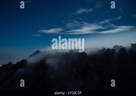 Vue nocturne de fumée sulfureuse du volcan Merapi sortant des rochers en silhouette noire Banque D'Images